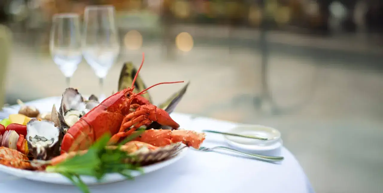 Wykwintna restauracja z owocami morza w Warszawie. Na talerzu homar, ostrygi i krewetki, obok kieliszki do wina.