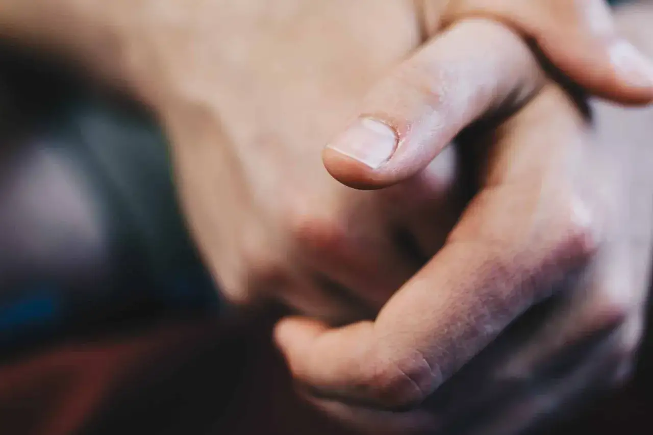 Gros plan sur un ongle homme, propre et bien entretenu, sur un fond flou de mains jointes.