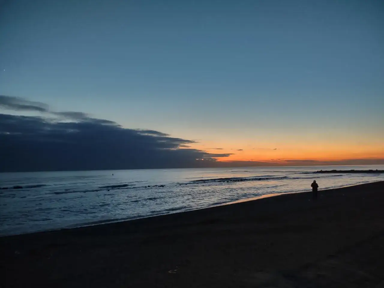 Zachód słońca nad morzem. Samotna postać na plaży, w oddali widać falochrony. Czy Rzym leży nad morzem? Tak, jego wybrzeże to Ostia.