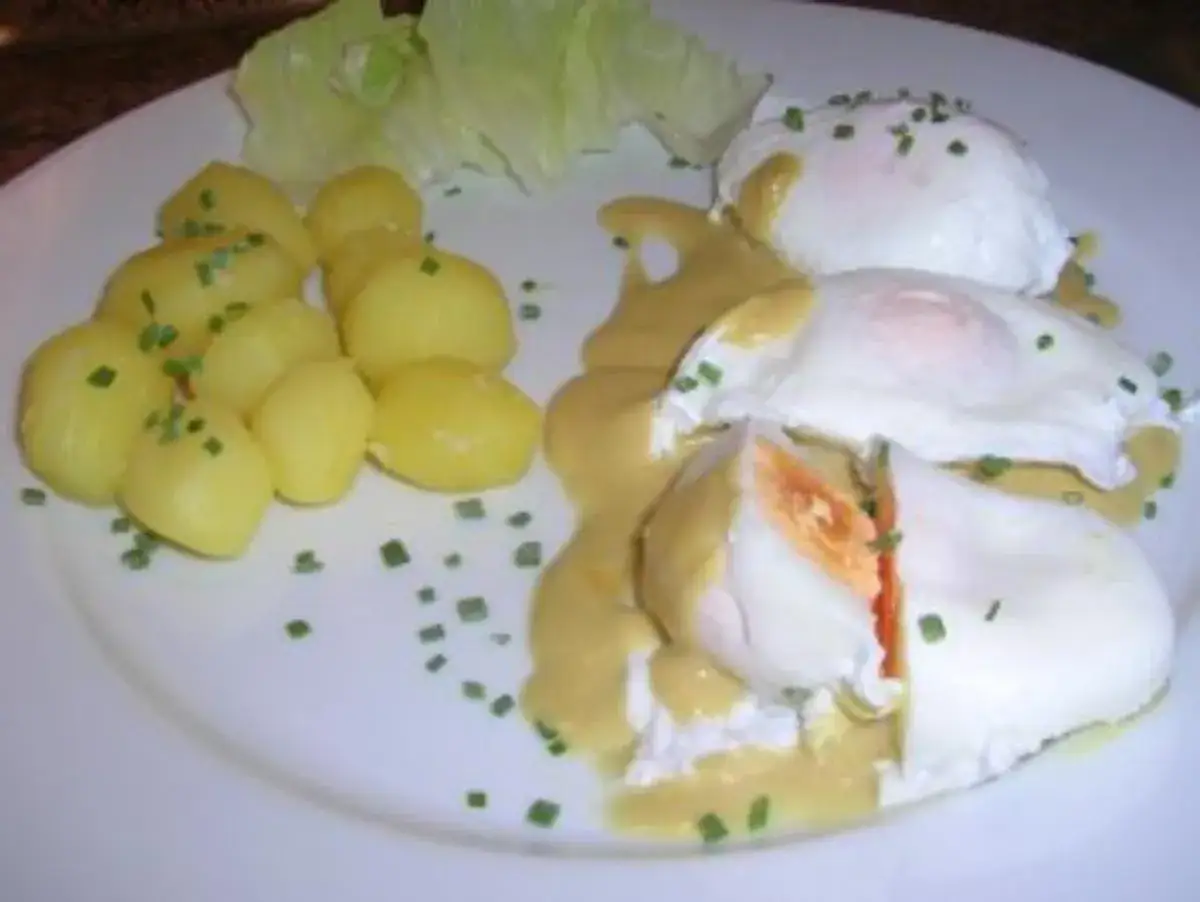 Verlorene Eier mit Sauce Hollandaise und kleinen Kartoffeln, garniert mit Schnittlauch. Ein leckeres Frühstück.