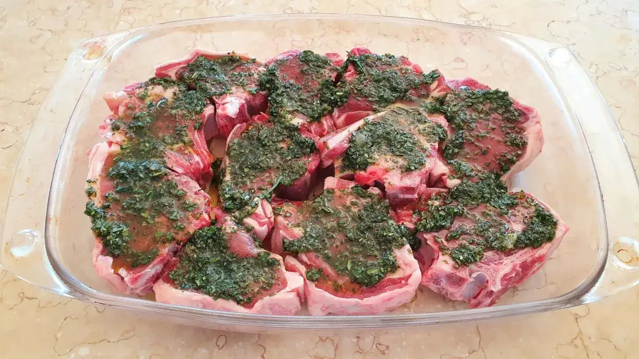 Plusieurs c&ocirc;telettes d'agneau crues, pr&ecirc;tes pour la cuisson, baignent dans une marinade verte et savoureuse.
