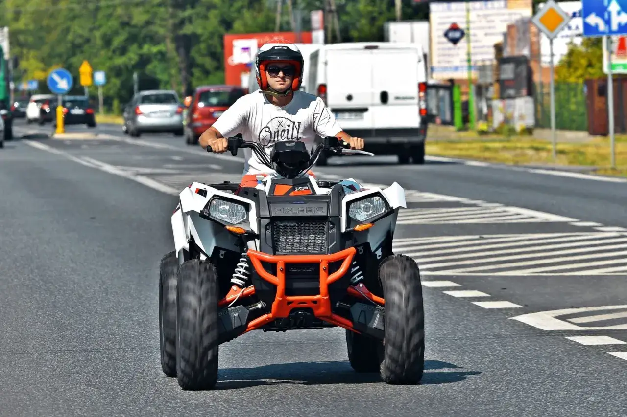 Mężczyzna w kasku jedzie quadem. Taki pojazd nie może wjechać na autostradę, bo jest zbyt wolny i niebezpieczny dla innych kierowców.