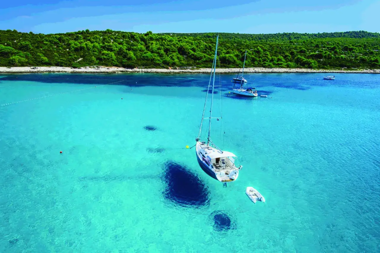 Vela bianca in acque cristalline, con altre barche all'ancora. Un paradiso tra le spiagge Croazia.