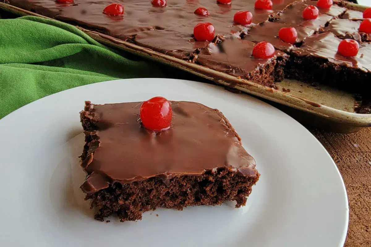 Ein Stück saftiger Schoko Kirsch Kuchen vom Blech, glasiert und mit Kirschen dekoriert.