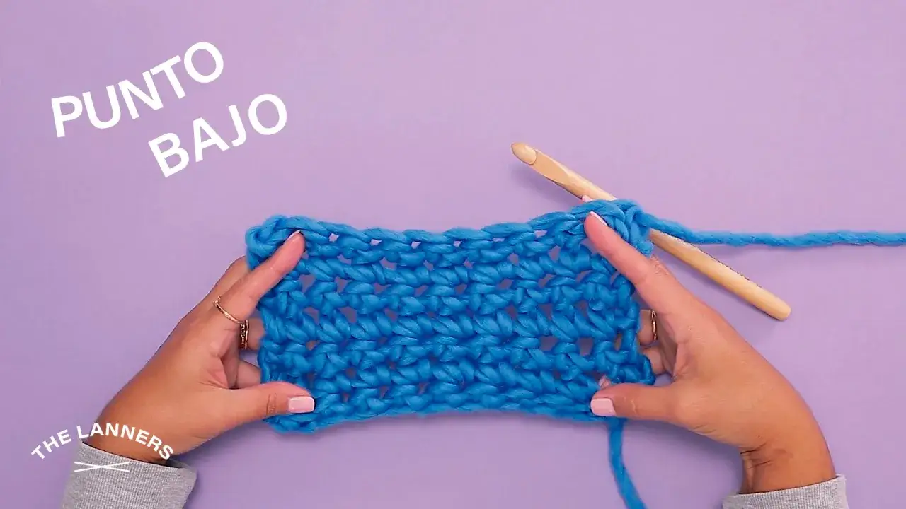 Manos tejiendo con ganchillo un tejido azul con el texto 