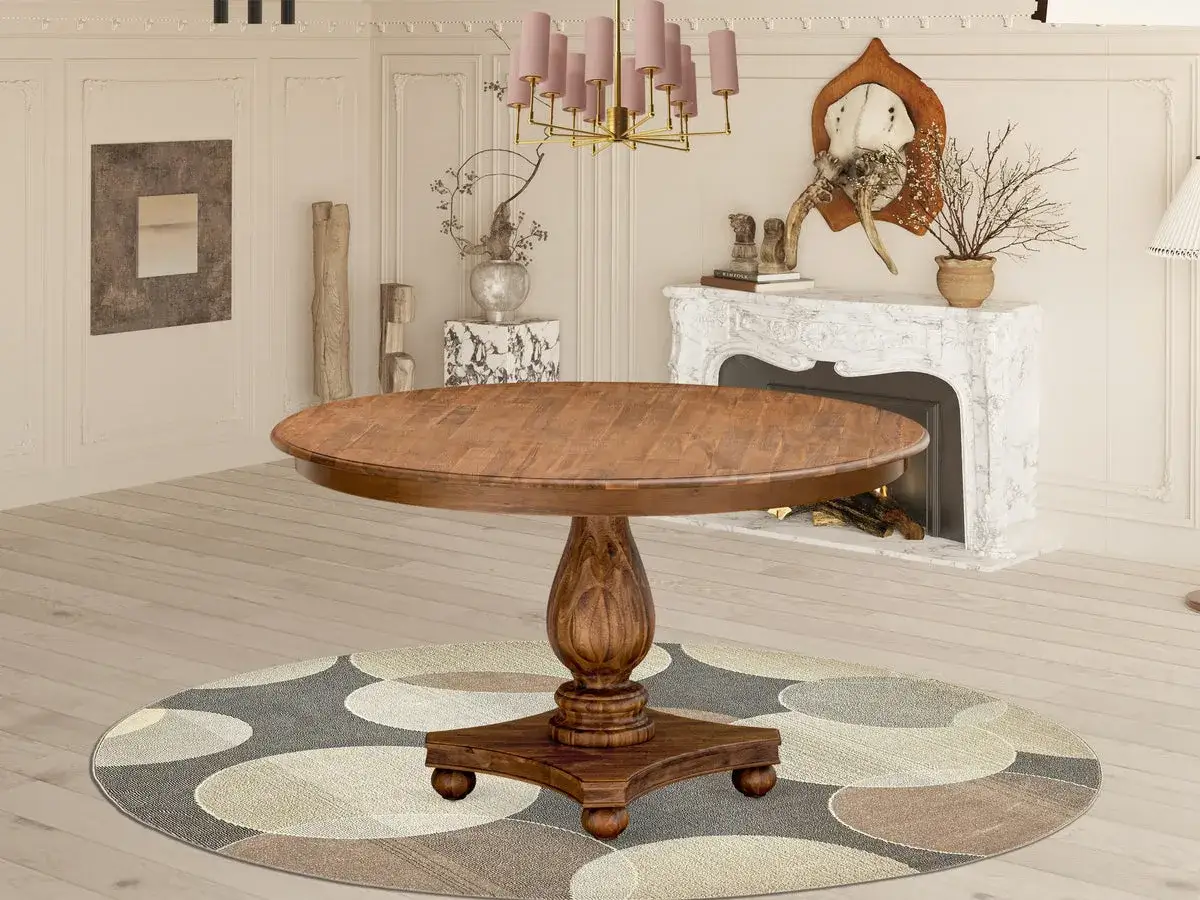 A round acica wood dining table with a pedestal base sits on a circular rug in a room with a fireplace and artwork.