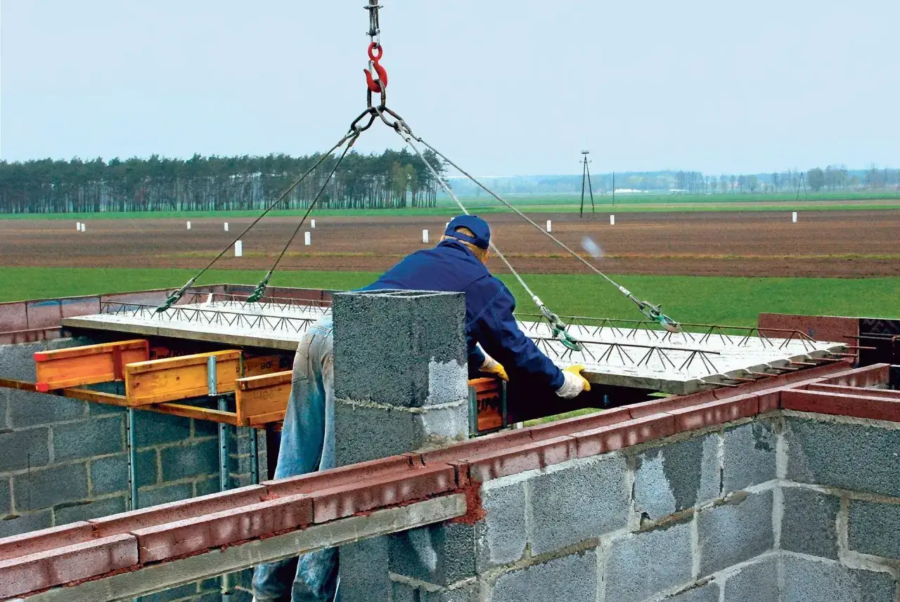 Robotnik kieruje opuszczaniem stropu filigran, który jest podnoszony przez dźwig.