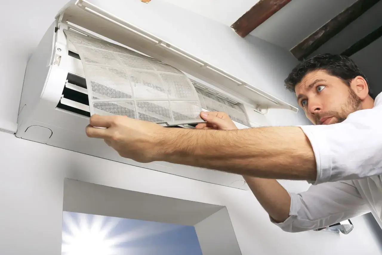 Un homme nettoie le filtre d'une climatisation. L'entretien climatisation tous les combien est une question importante pour la qualit&eacute; de l'air.