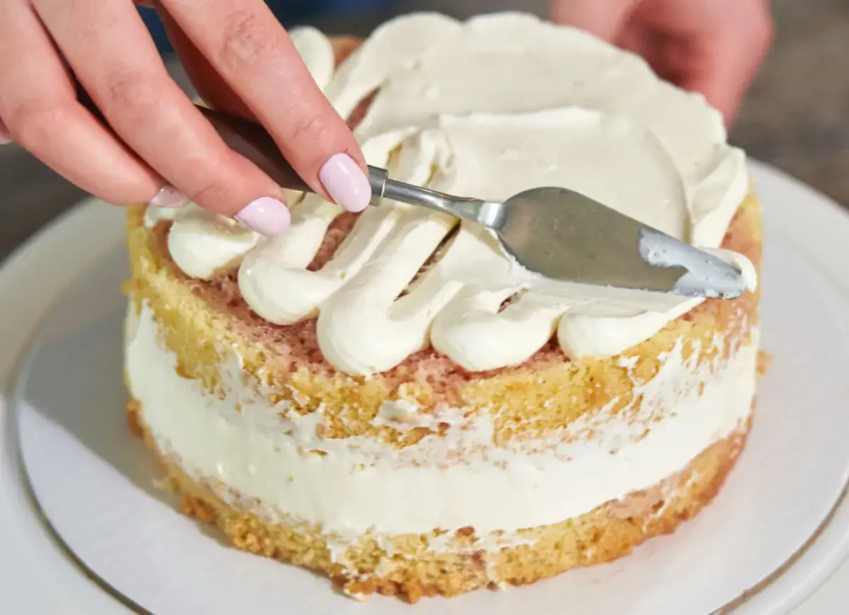 Ręce dekorują tort, rozprowadzając puszystą masę budyniową z mascarpone.