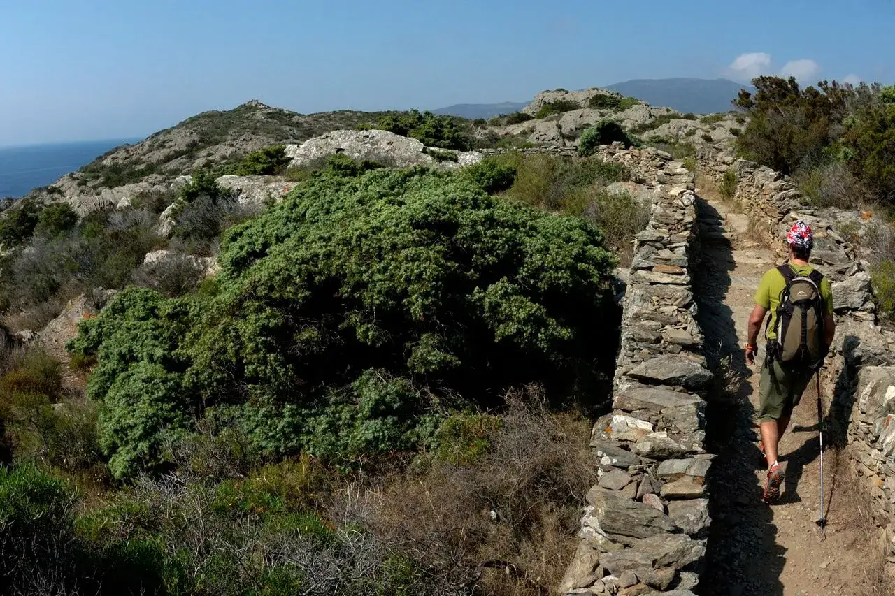 Senderista en un camino de piedra con vistas al mar, explorando una de las mejores rutas de senderismo de Espa&ntilde;a.