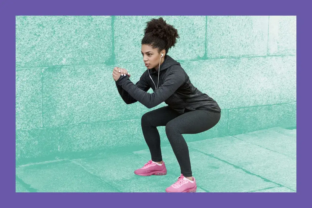 Donna con cuffie fa squat, un esercizio che fa dimagrire, contro un muro verde.