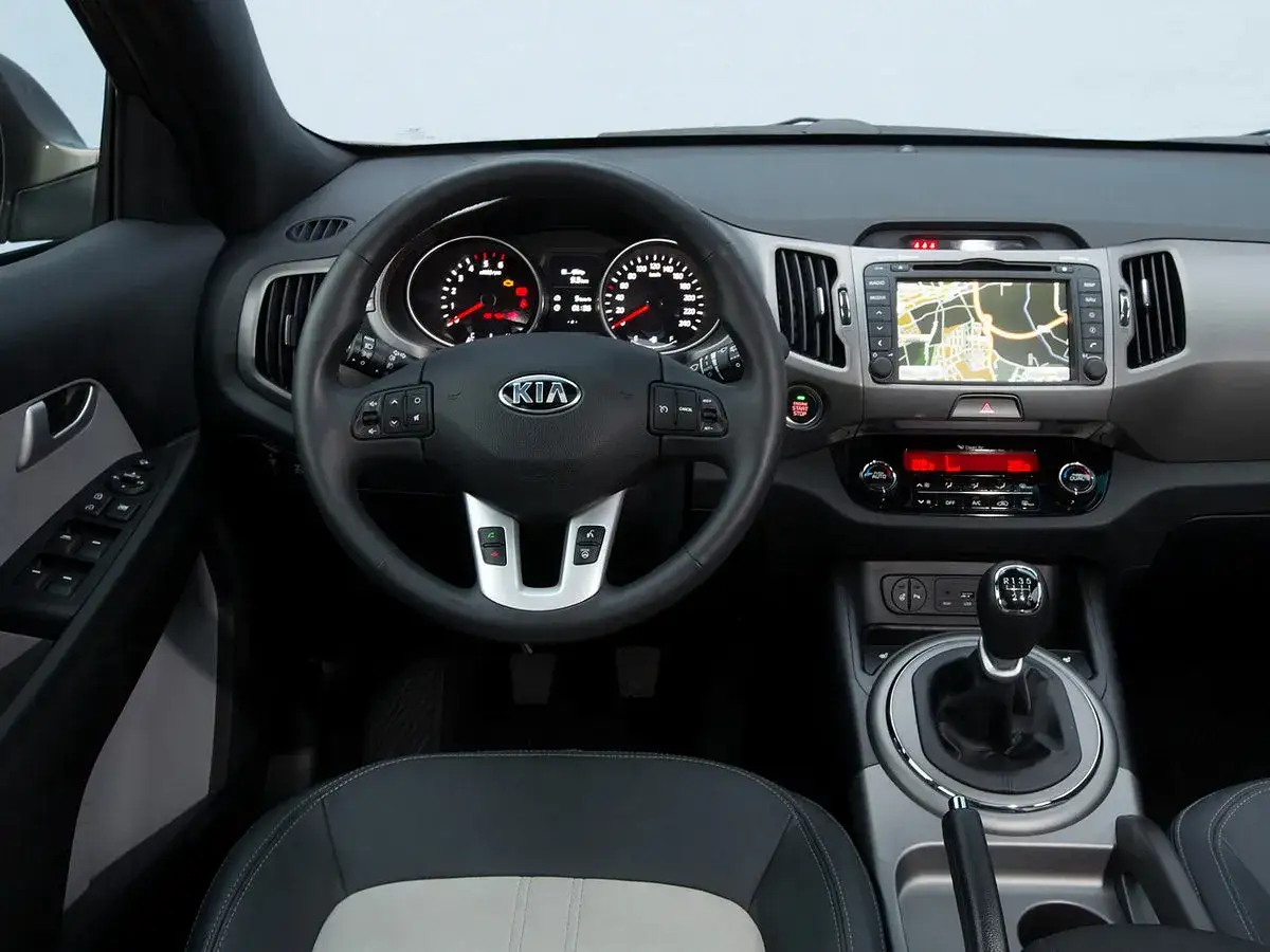 Wnętrze Kia Sportage 2015: kierownica, deska rozdzielcza z nawigacją i panelem klimatyzacji, dźwignia zmiany biegów.