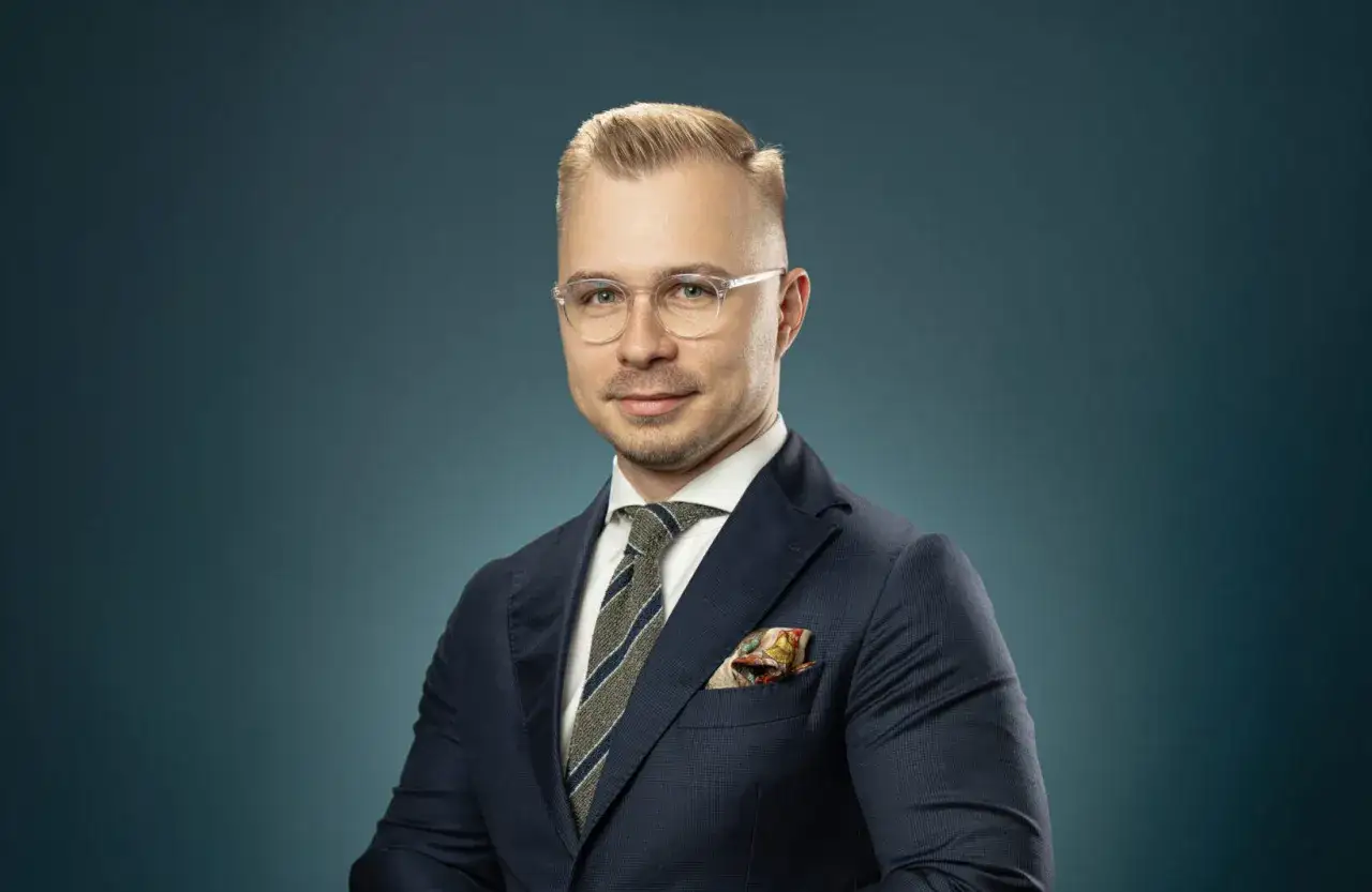 Portret mężczyzny w garniturze, okularach i krawacie, na tle granatowym.
