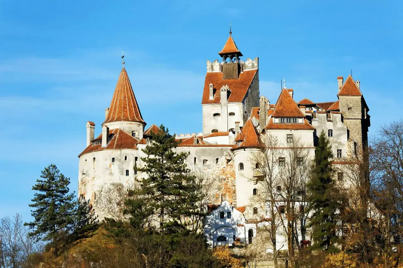 Dracula zamek, majestatyczna twierdza na wzgórzu, z czerwonymi dachami i wieżami, otoczona drzewami.