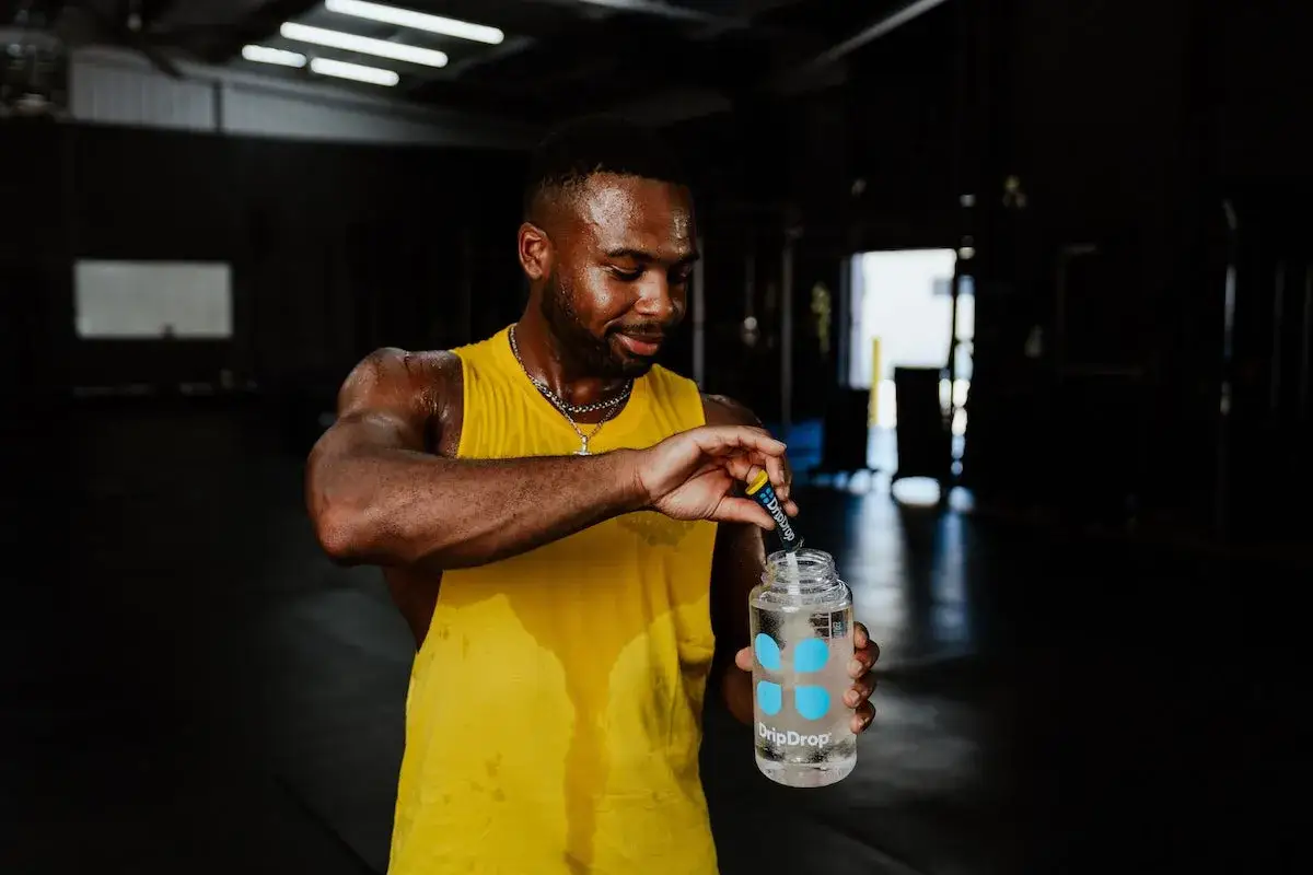 Schwitzender Mann im Fitnessstudio gibt Tropfen in seine Wasserflasche. Er bereitet sich mit dem richtigen Salz vor dem Training vor.