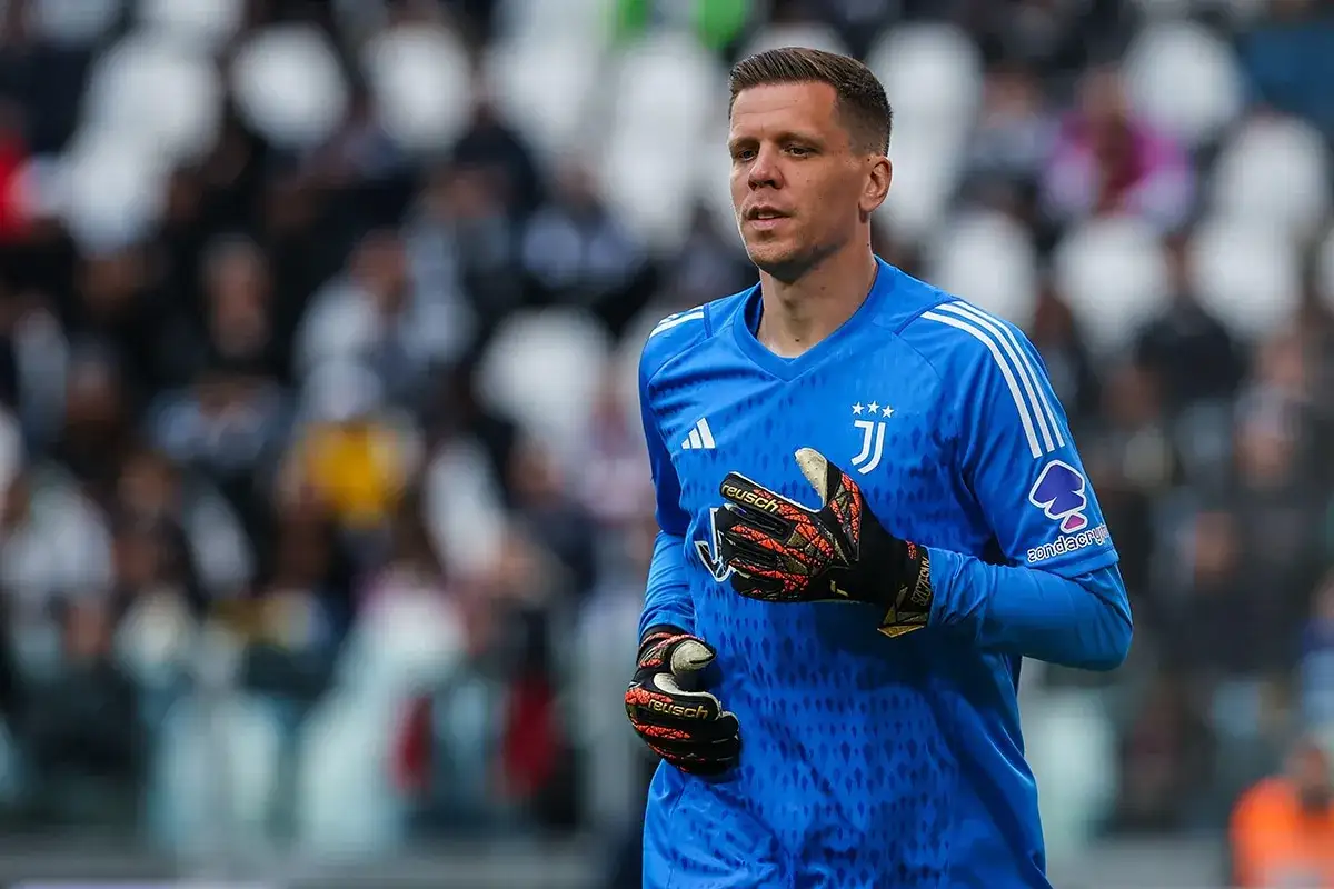Wojciech Szczęsny w bramce Juventusu. Bramkarz w niebieskiej koszulce z herbem klubu, gotowy do akcji na boisku.