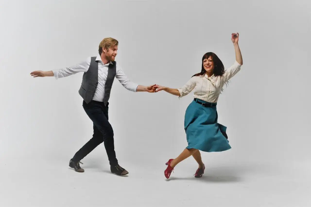 Coppia balla swing, uomo con gilet e donna con gonna svolazzante. La differenza tra swing e lindy hop &egrave; evidente nel loro dinamismo.