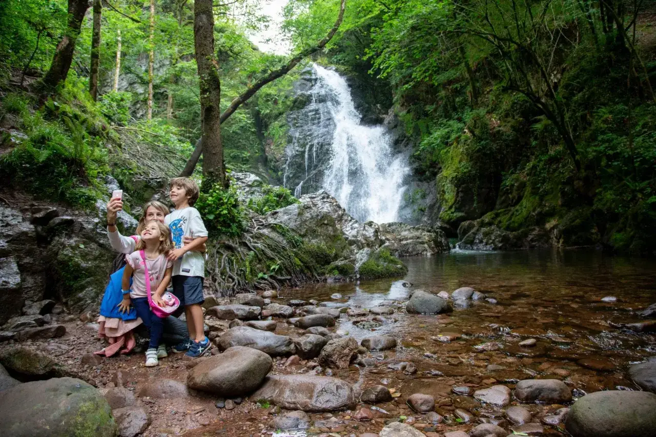 Familia toma selfie frente a la imponente cascada Xorroxin, rodeada de exuberante vegetación y rocas.