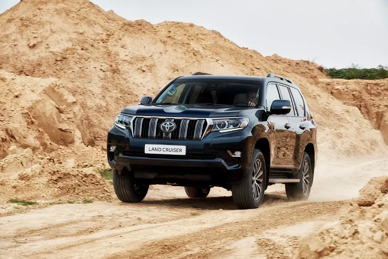 Czarny Land Cruiser Prado pokonuje piaszczysty teren, wzbijając tumany kurzu.