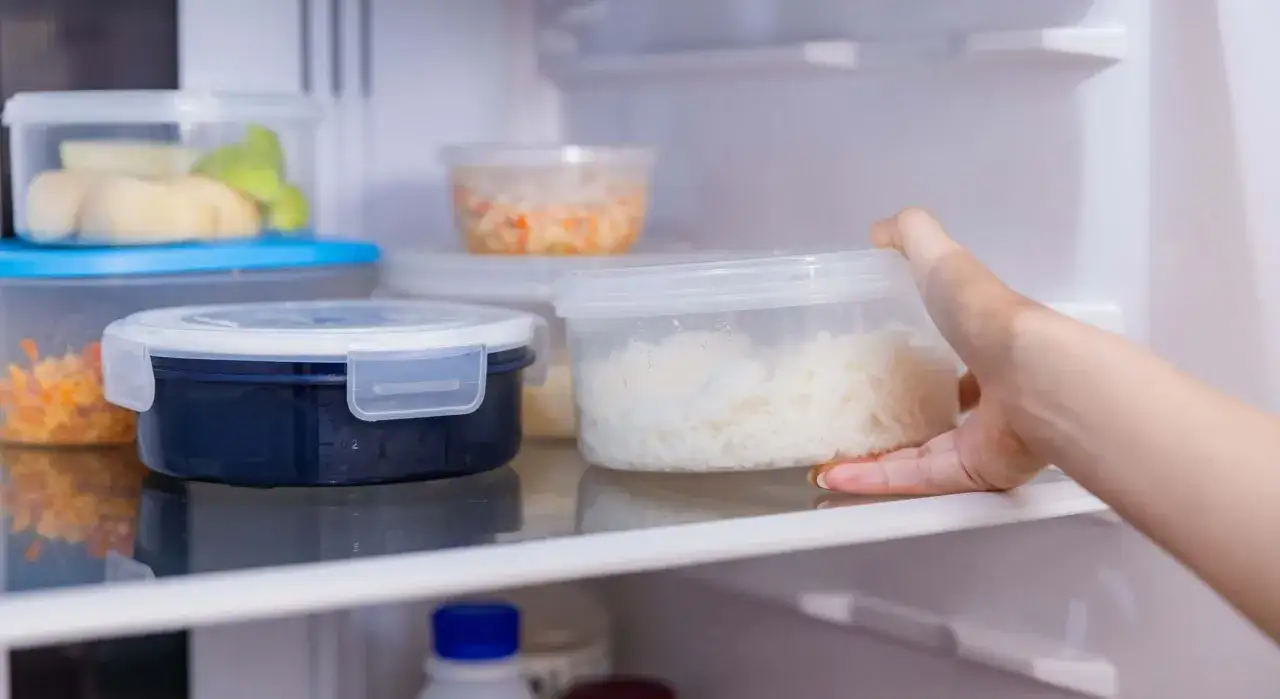 Mano saca un recipiente con arroz blanco de la nevera. Averigüemos cuanto dura el arroz en la nevera.