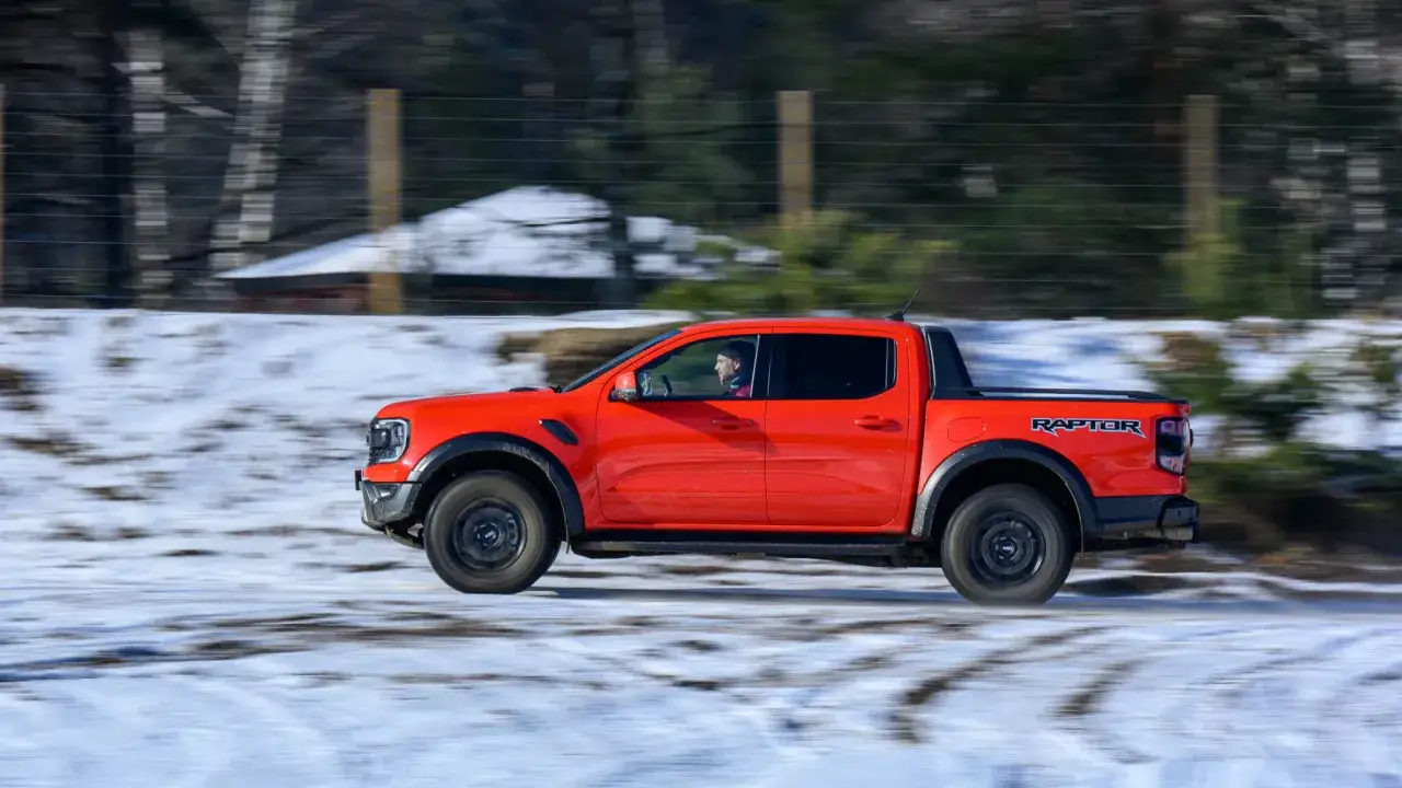 Pomarańczowy Ford Ranger Raptor pędzi po zaśnieżonej drodze, kierowca w kabinie.