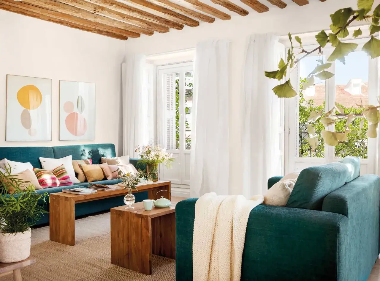 Acogedor salón con sofá verde, vigas de madera en el techo y mucha luz natural.