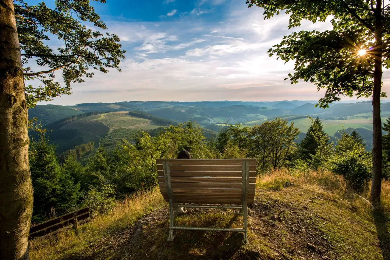 Ein Mensch sitzt auf einer Bank und blickt in eine weite H&uuml;gellandschaft. Ein Ort, der zum Innehalten einl&auml;dt, ein wahrer weg der sinne.