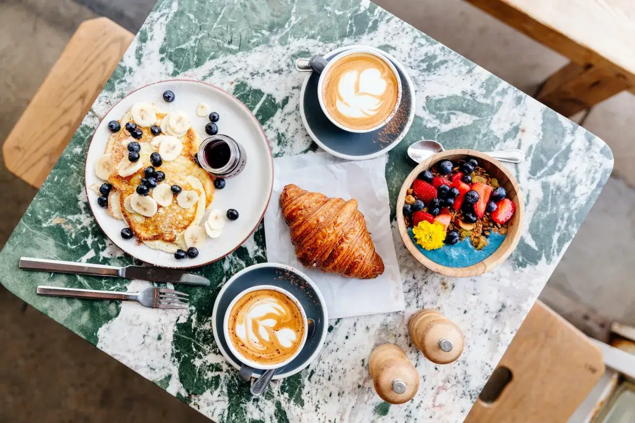 Pyszne naleśniki z bananami i jagodami, croissant, owsianka z owocami i dwie kawy latte. Idealny deser zamiast kolacji.