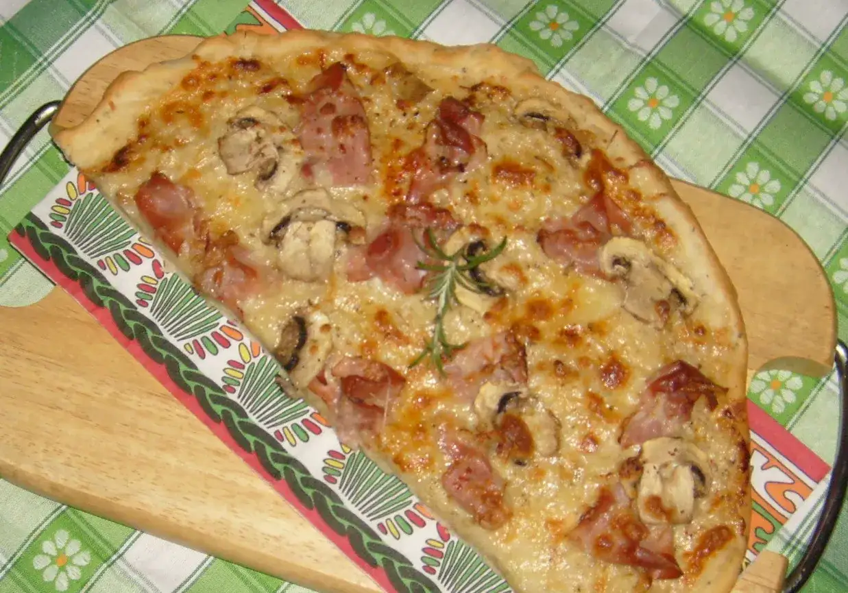 Pyszna pizza carbonara z szynką, pieczarkami i rozmarynem, podana na drewnianej desce.