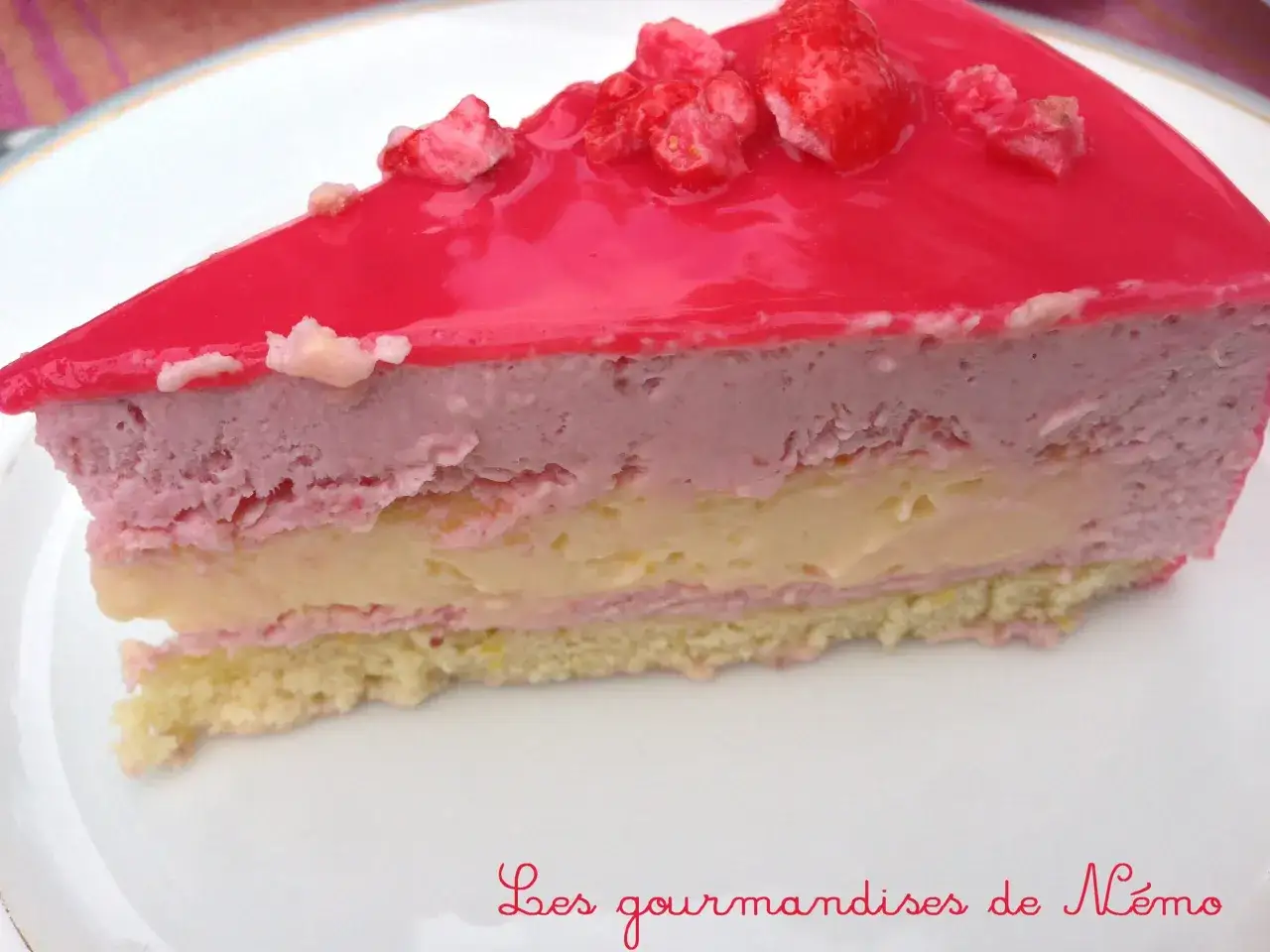 Tranche d'entremet fraise, rose et jaune, sur une assiette blanche. Délicieux et gourmand !