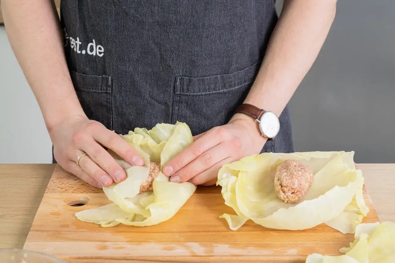 H&auml;nde formen Kohlrouladen. Ein Hackfleischkl&ouml;&szlig;chen liegt auf einem Kohlblatt, bereit f&uuml;r das Einrollen. Das Kohlrouladen Rezept wird hier vorbereitet.