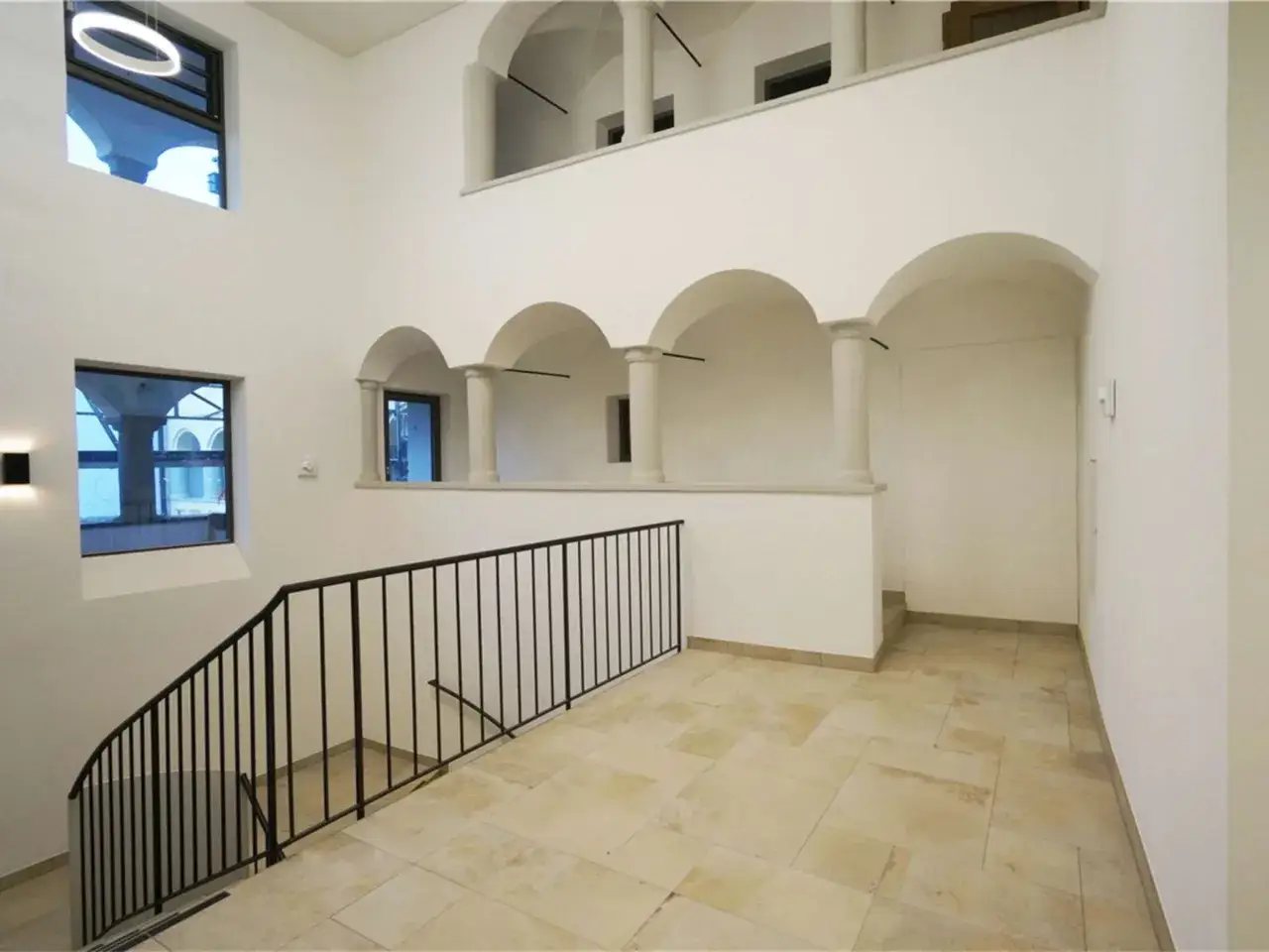 Innenansicht des bischof bernhard haus kraiburg mit einer geschwungenen Treppe, Bögen und Säulen.