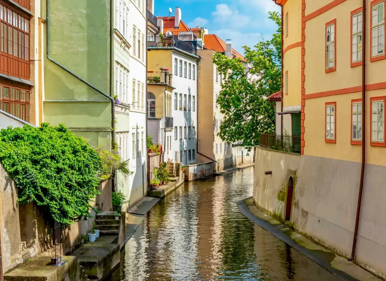 Malerischer Kanal in Prag, ein idyllisches Motiv für Ausflugsziele. Bunte Häuser säumen das Wasser, üppiges Grün rankt sich an den Mauern empor.