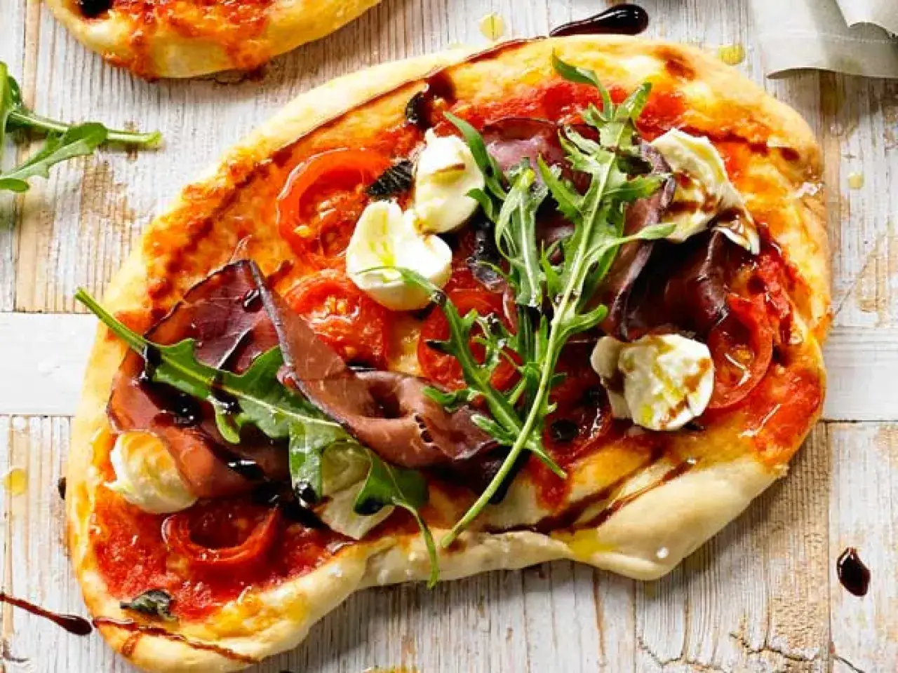 En l&auml;cker bresaola pizza med tomater, mozzarella och ruccola, ringlad med balsamvin&auml;ger.