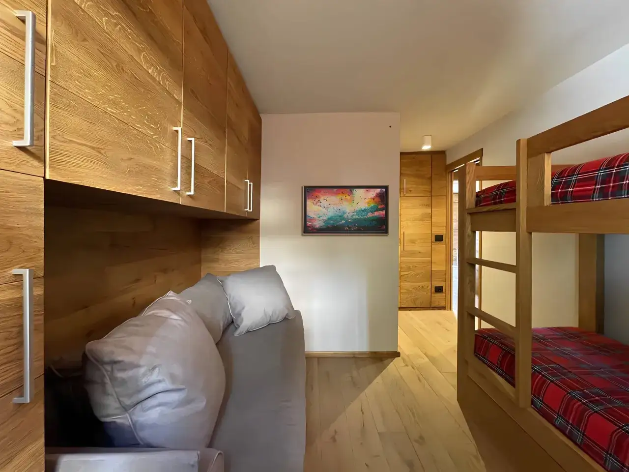 Accogliente camera con letti a castello e divano, un esempio di **idee piccole case di montagna** con arredi in legno e un quadro colorato.
