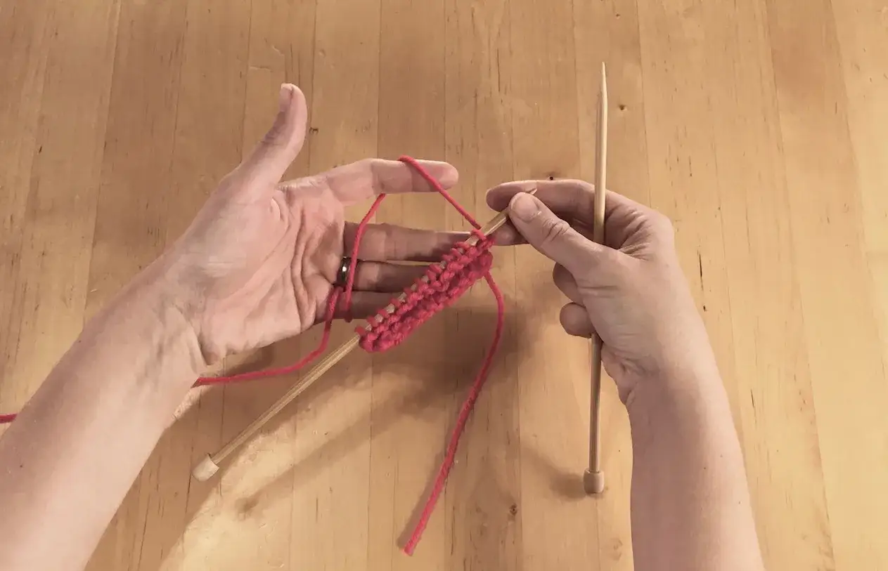 Mani che lavorano a maglia con filato rosa e ferri di legno.
