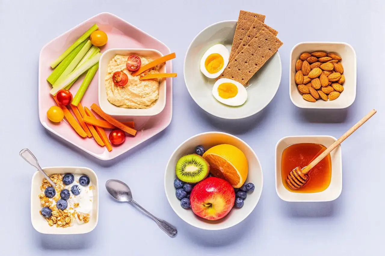 Zdrowe przekąski w ciąży: jogurt z jagodami, hummus z warzywami, jajka, owoce, orzechy i miód.