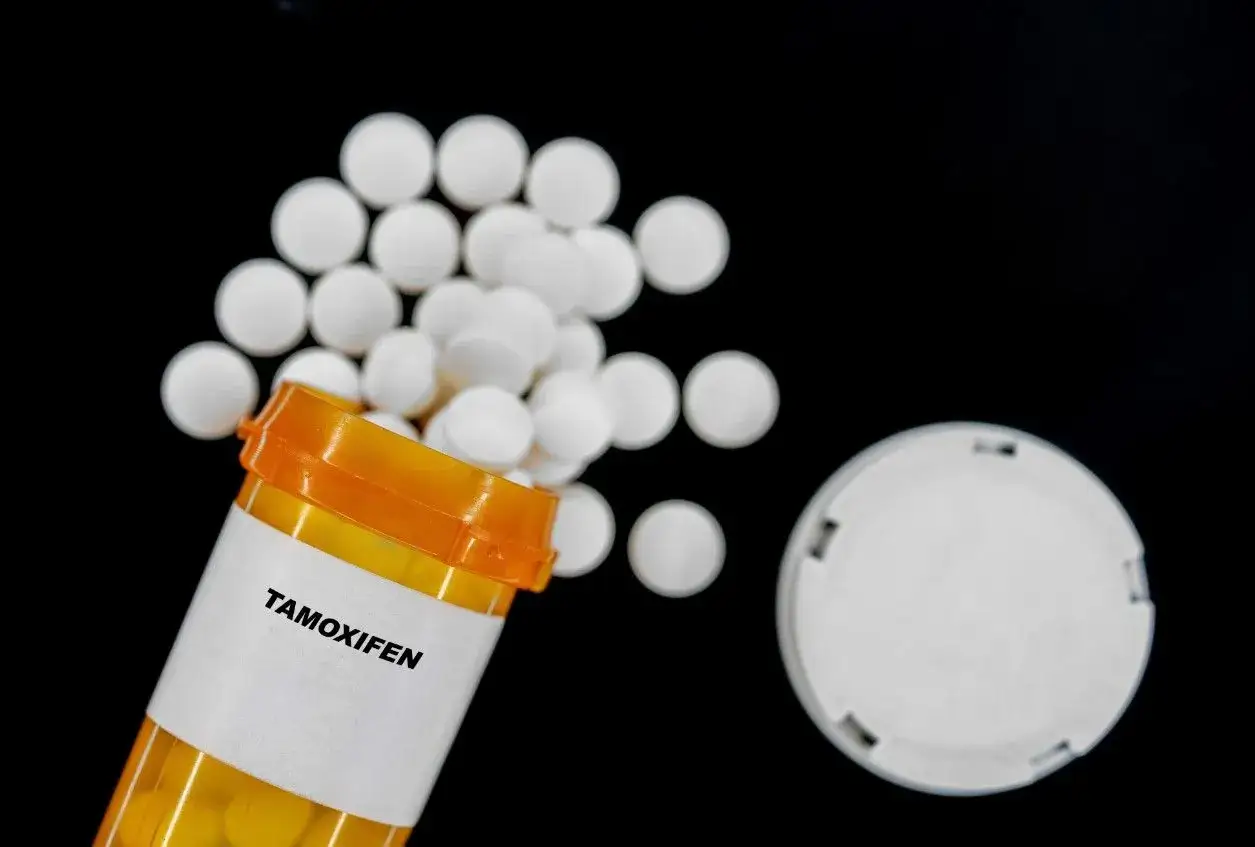 Butelka z tabletkami tamoxifen, rozsypane białe pigułki na czarnym tle.