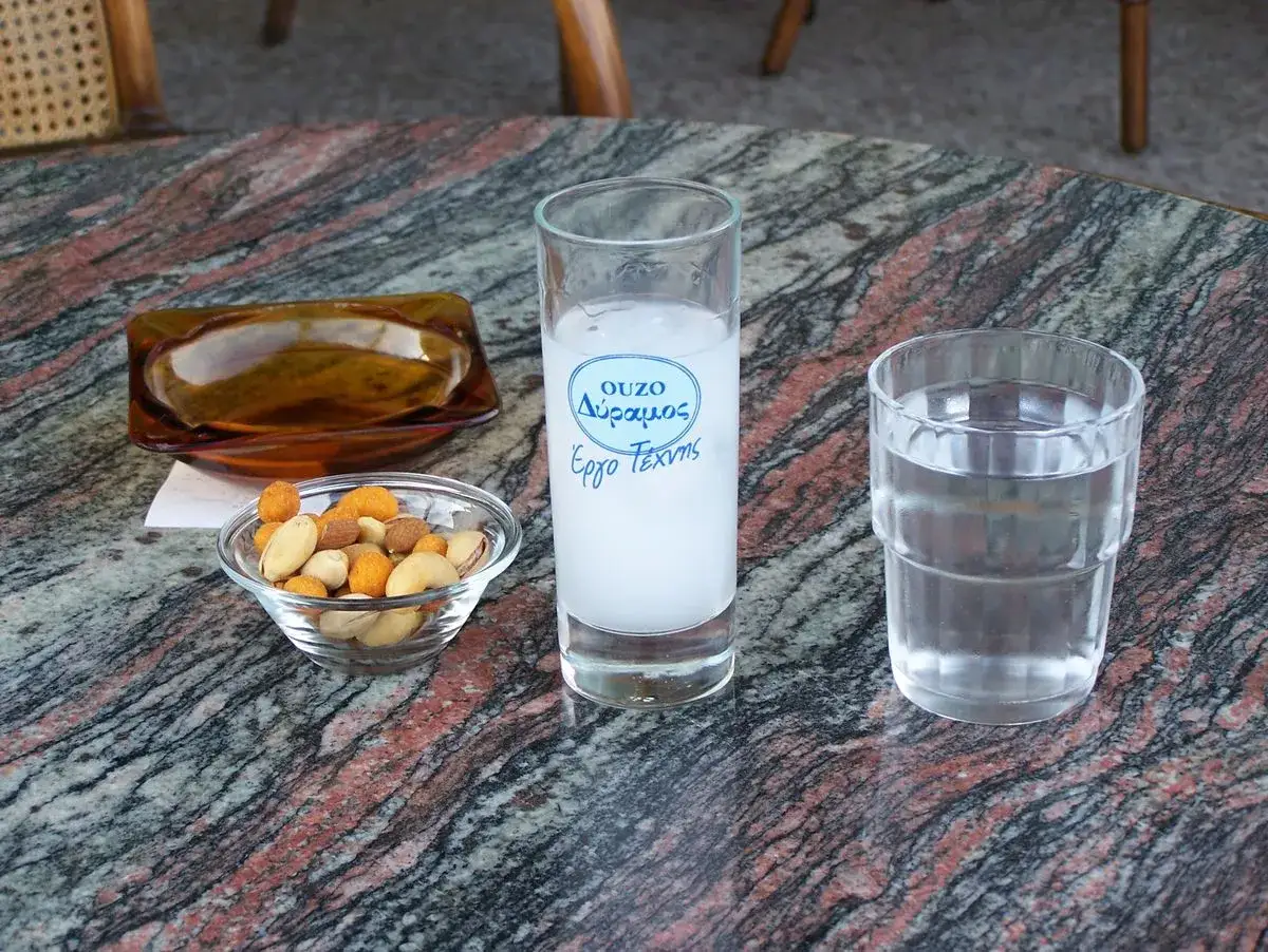 Ein Glas Ouzo mit Wasser und eine Schale N&uuml;sse auf einem Marmortisch.