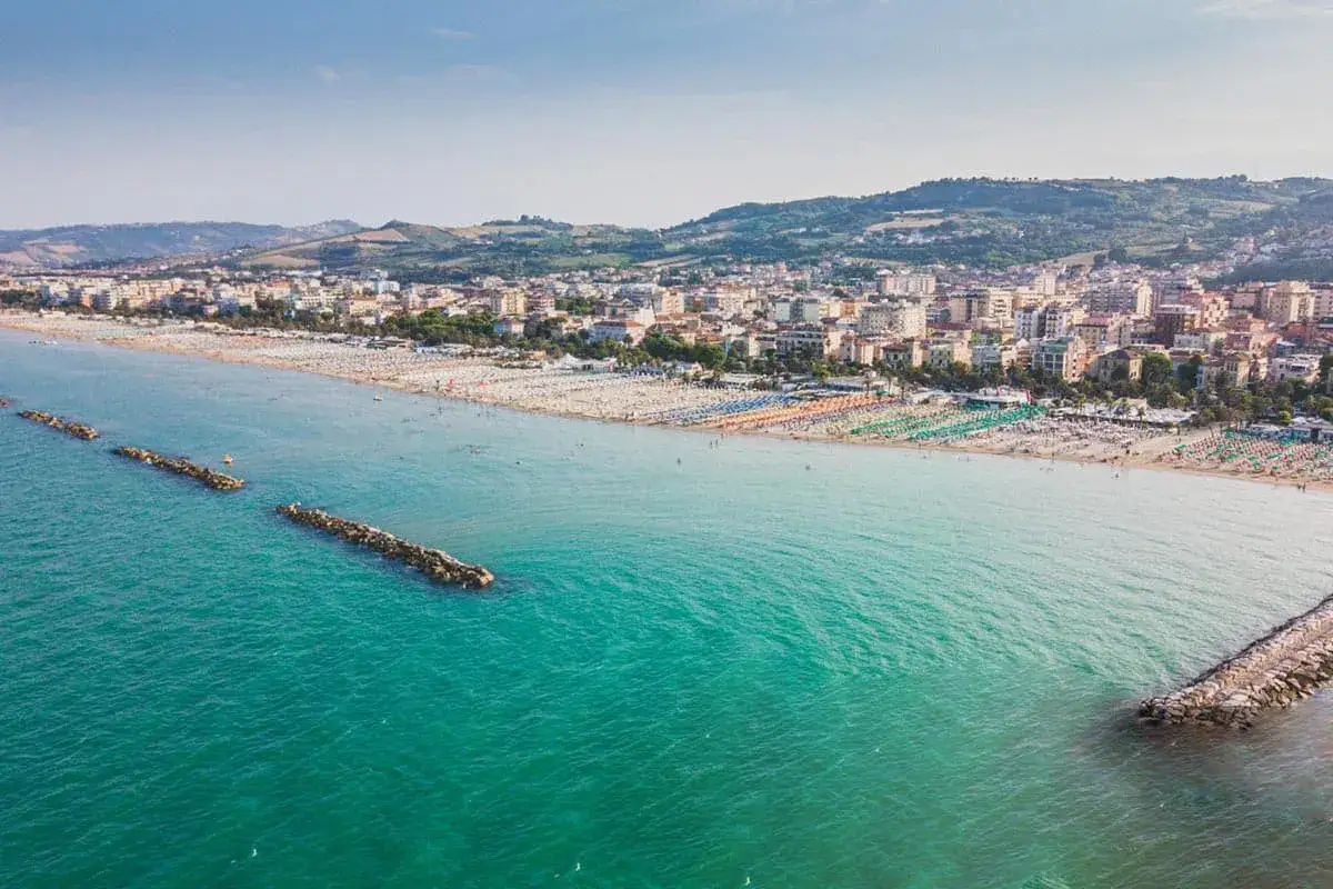 Le spiagge di San Benedetto del Tronto, con file ordinate di ombrelloni colorati e il mare azzurro, si estendono fino alla città.
