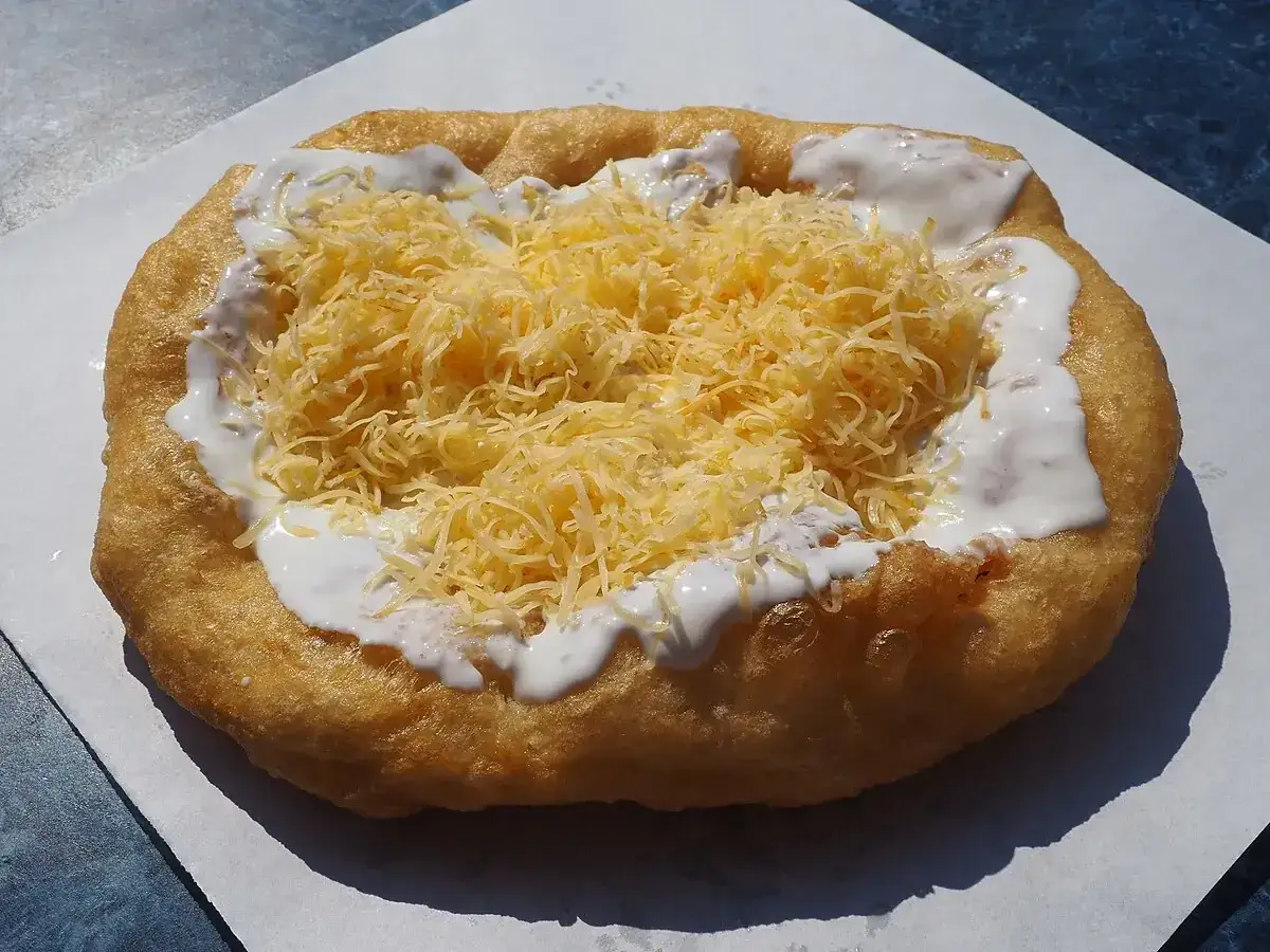 Lángos, un delicioso bocado para comer en Budapest, cubierto con queso rallado y crema agria.