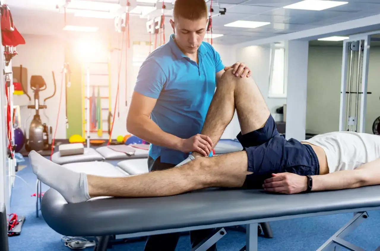 Fisioterapista assiste paziente in riabilitazione crociato anteriore, con esercizi mirati al ginocchio su lettino in palestra.