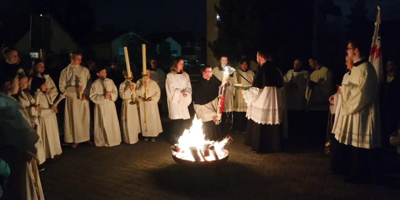 Feuer und Kerzen beleuchten die Nacht. Eine Gruppe in wei&szlig;en Gew&auml;ndern und Geistliche versammeln sich. Dies ist die Feier der Osternacht.