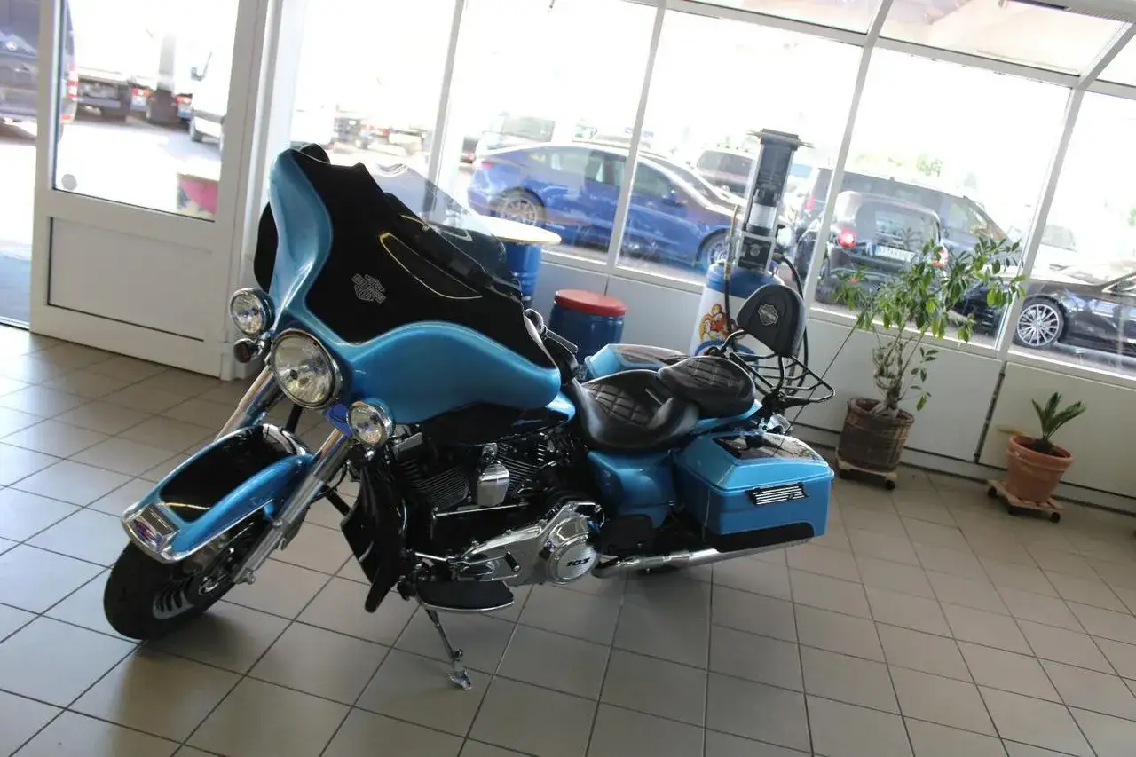 Błękitny motocykl Harley-Davidson w salonie. W tle widać inne samochody i ciężarówki, jak na niemieckich stronach z motocyklami.