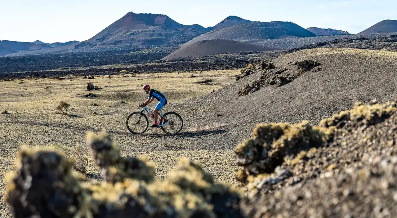 Ciclista pedaleando por un paisaje volcánico en Lanzarote en bici. Montañas y rocas cubren el horizonte.