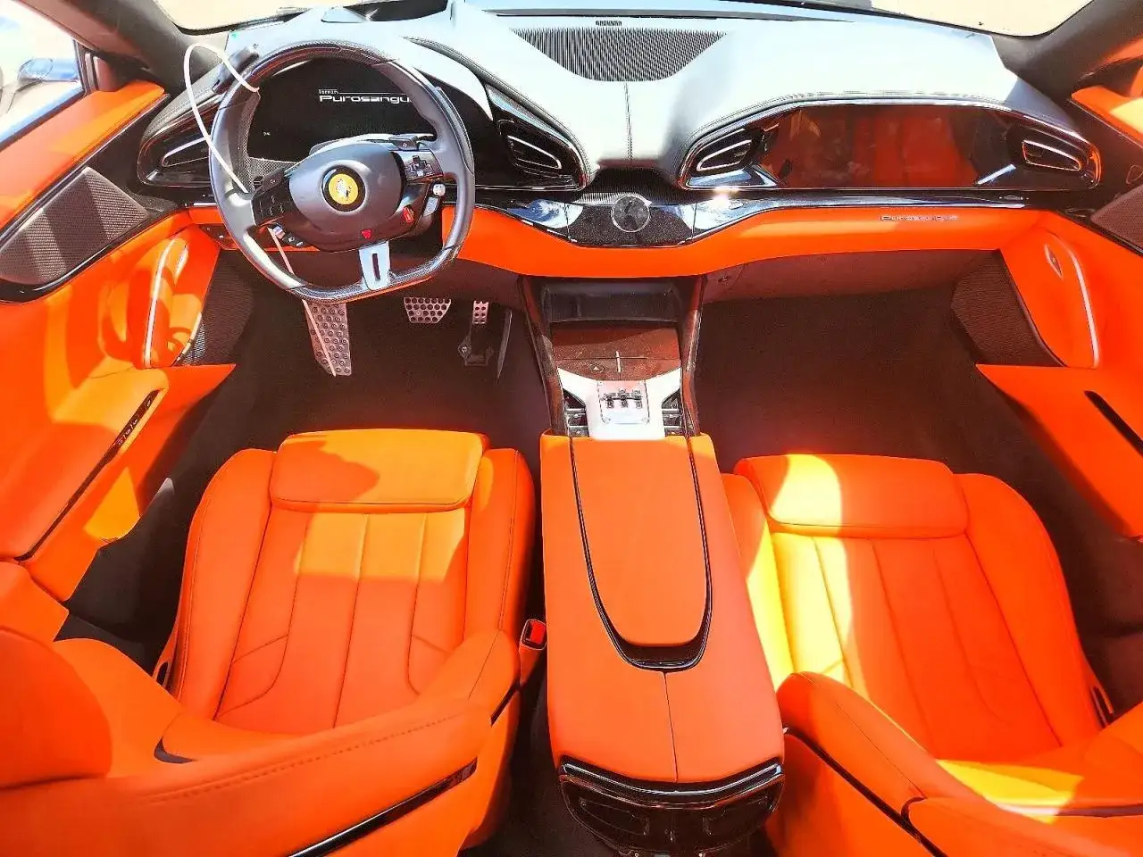 Wnętrze Ferrari Purosangue w jaskrawym kolorze pomarańczowym. Skórzane fotele i deska rozdzielcza tworzą luksusową atmosferę.
