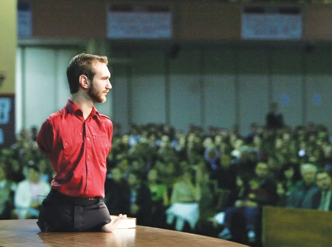 Nick Vujicic, ohne Arme und Beine, steht auf einer Bühne vor einem Publikum und spricht.