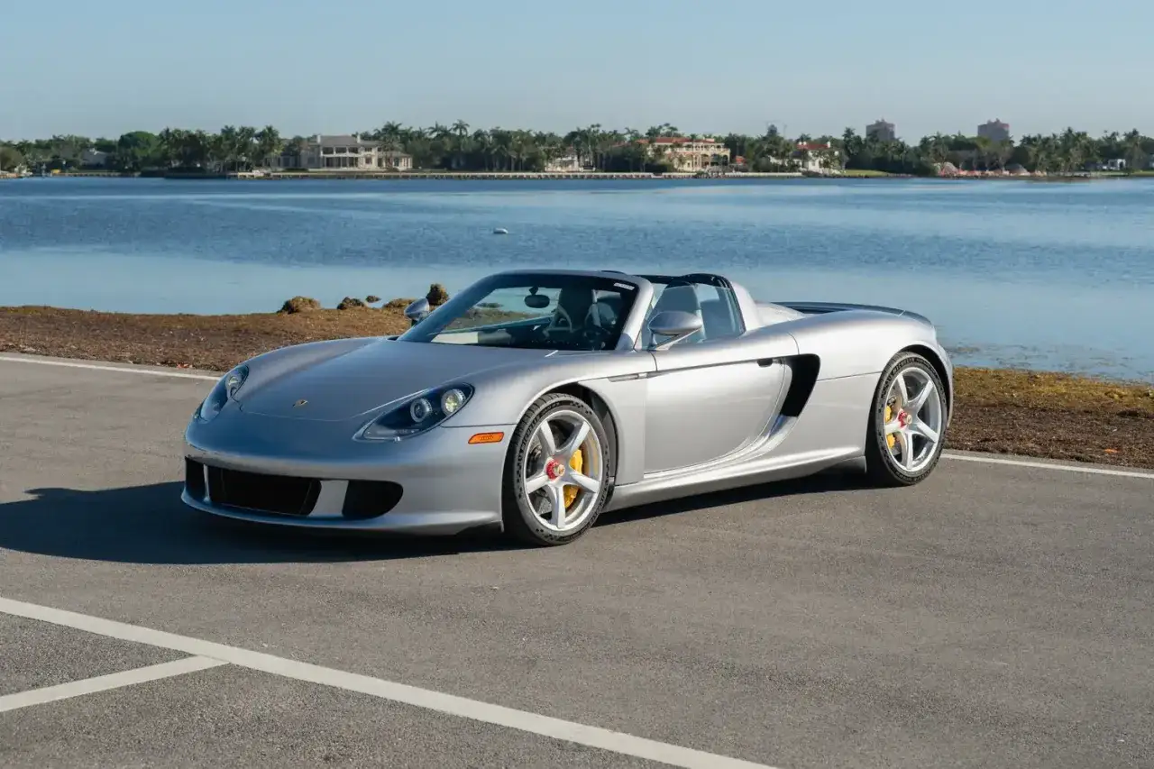 Silberner Porsche Carrera GT, offen, am Wasser geparkt. Ein Traumauto f&uuml;r sonnige Tage.