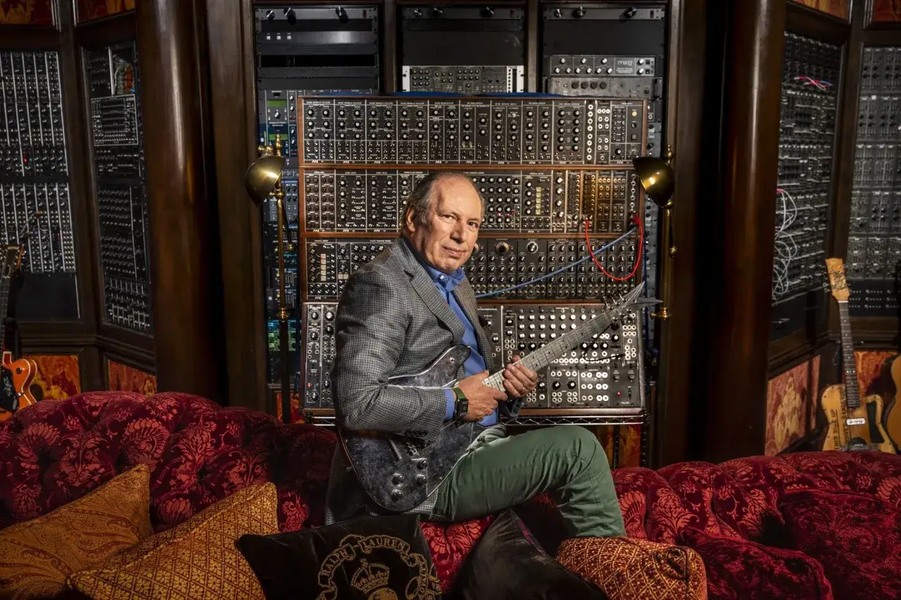 Hans Zimmer, twórca muzyki do wielu filmów, siedzi z gitarą w otoczeniu syntezatorów.