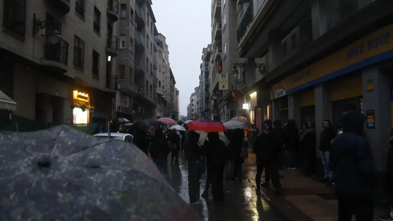 Gente con paraguas en una calle de Zaragoza, celebrando el solsticio de invierno bajo la lluvia.